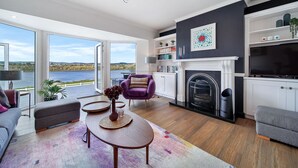 A modern living room with a fireplace, a sofa, a coffee table, and a view of the outdoors. - Fresh & Stylish | Ocean View | Donegal Town & Bay (Tullycullion)