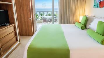 A hotel room with a bed, a TV, a balcony with a table and chairs, and a view of the ocean.
