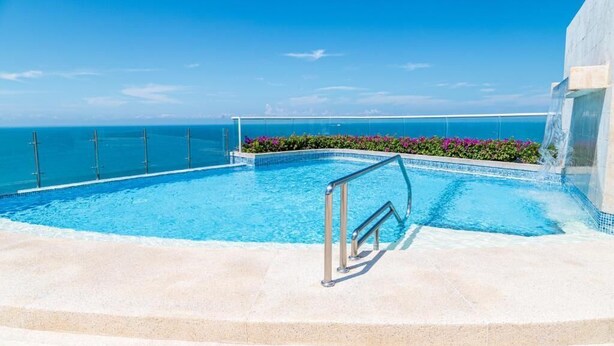 Piscina azul cristalina con vista al océano, rodeada por una terraza de concreto y barandillas de metal.