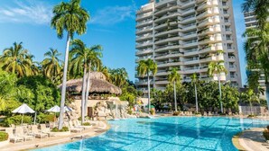 Un hotel con una piscina grande, palmeras y una estructura de techo de paja.