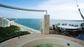 Un balcón con vistas a la playa y al océano, un jacuzzi y mobiliario exterior.