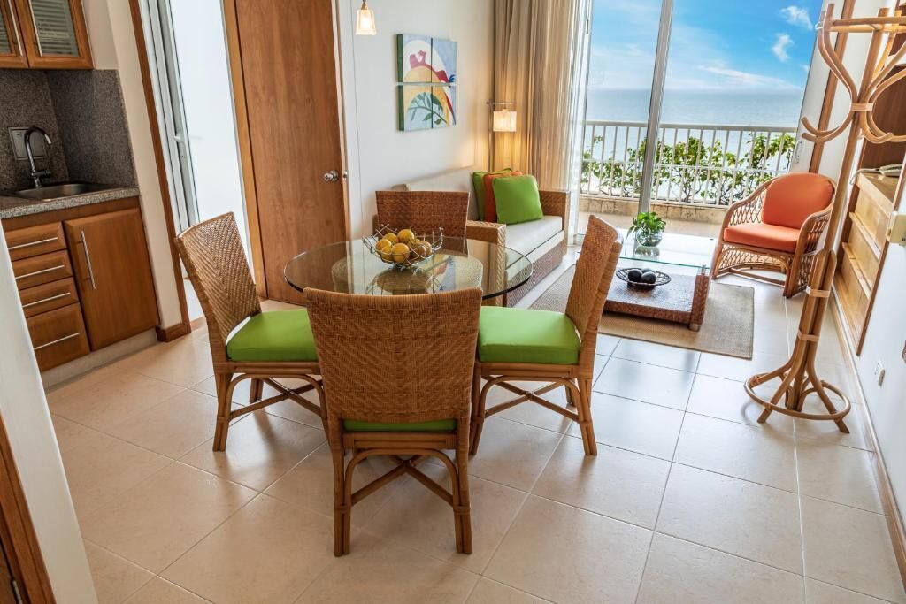 A dining area with wicker chairs and a glass table, a sofa with cushions, and a view of the sea.