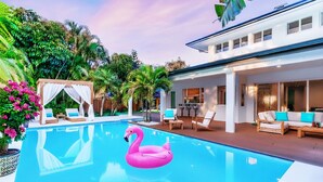 Uma piscina com um flutuador em formato de flamingo rosa, rodeada por mobiliário de área externa e vegetação exuberante.