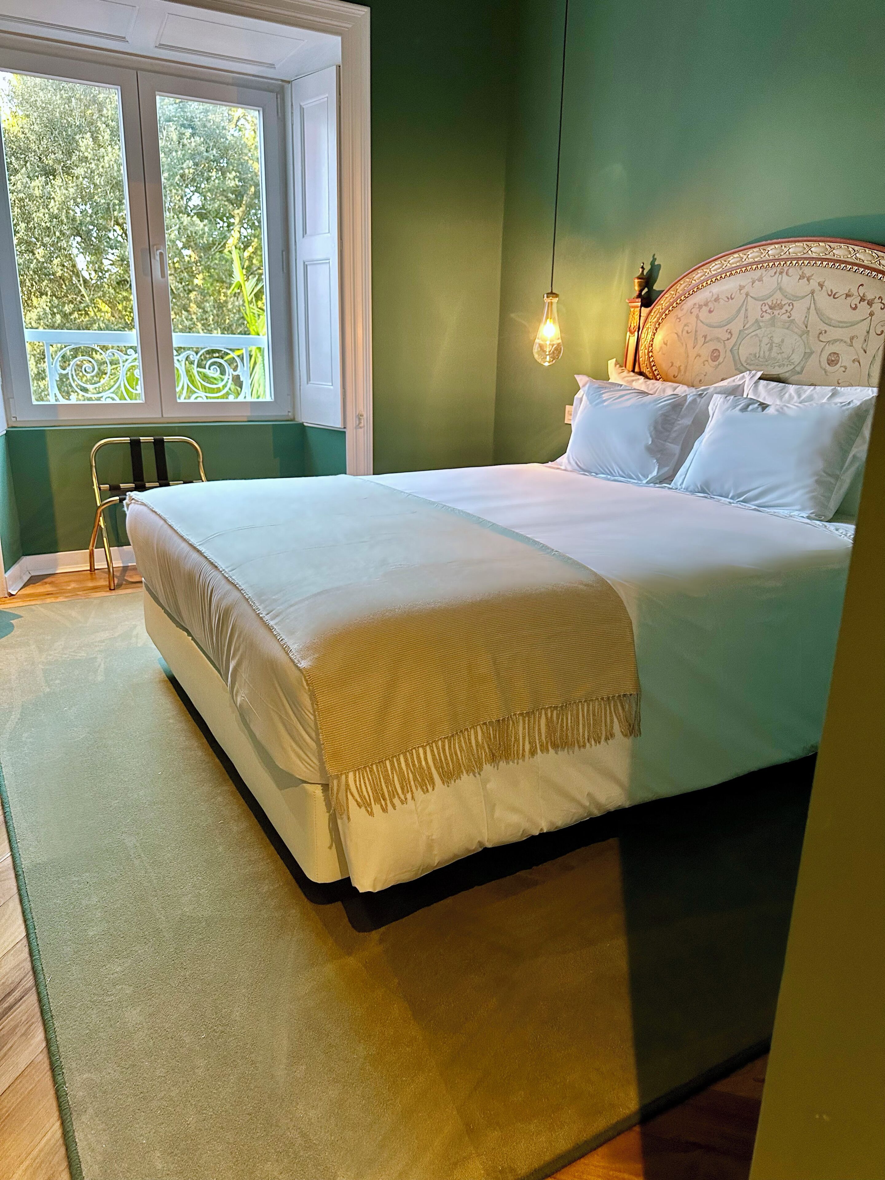 Een slaapkamer met een bed, een raam, een stoel en een hanglamp.