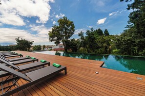 Una terraza de madera con sillones de descanso y una piscina.