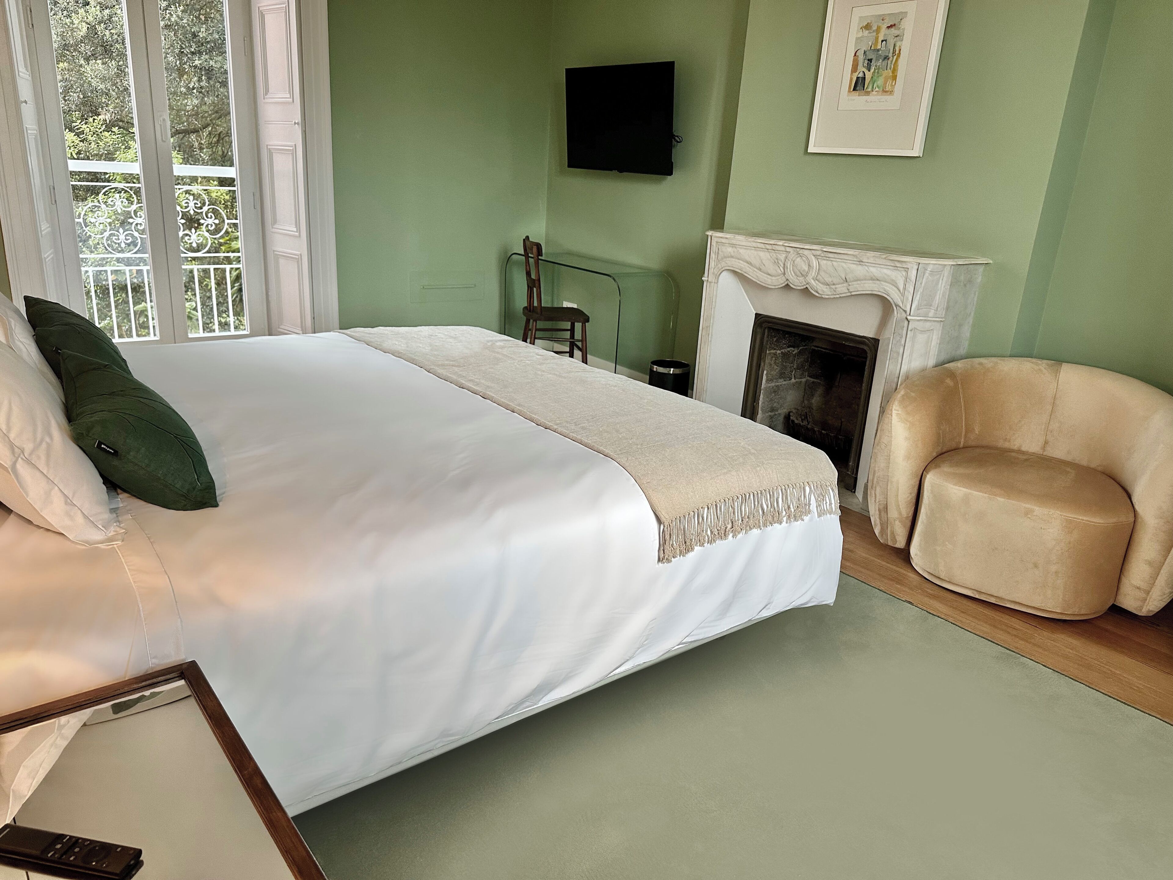 A bedroom with a bed, a chair, a fireplace, and a TV on the wall.