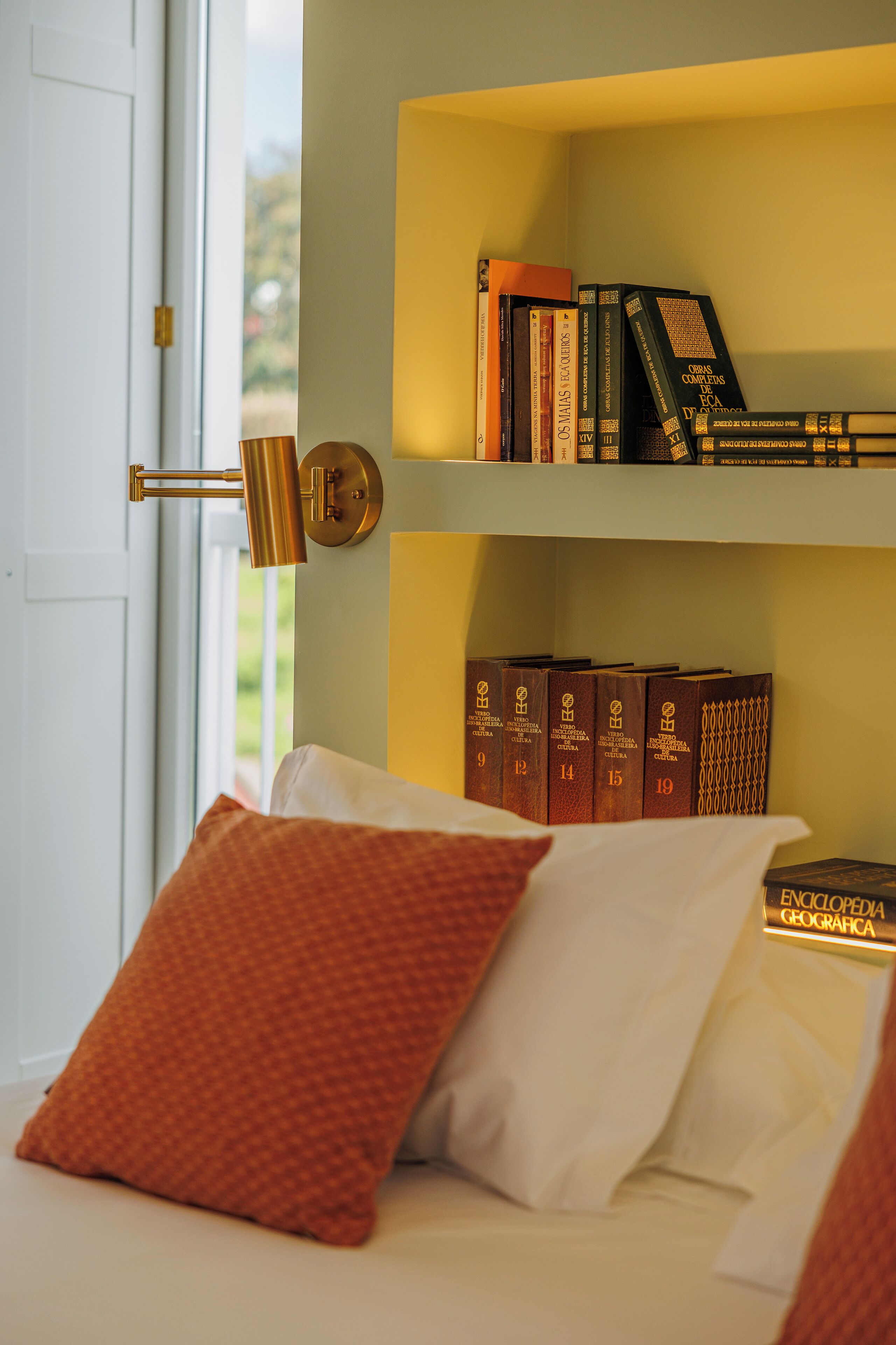 A neatly arranged bedroom with a bed, pillows, and a shelf with books.