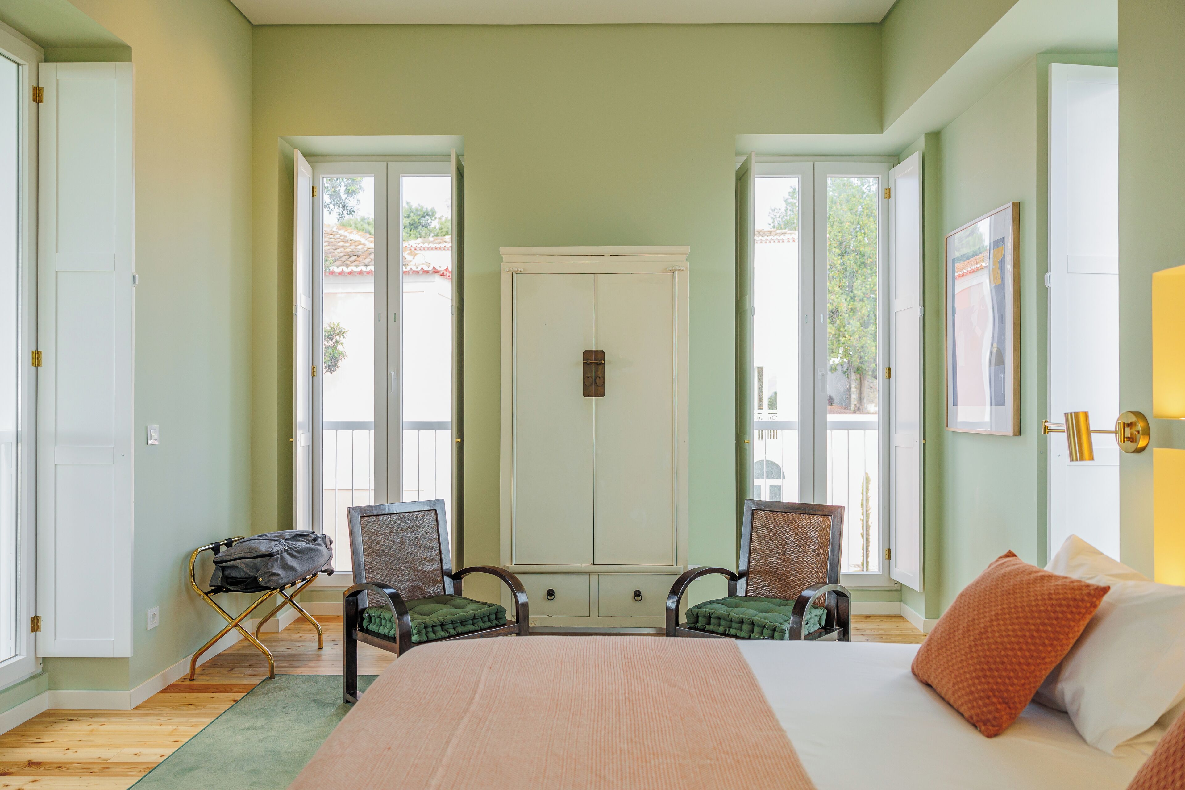 A bedroom with a bed, two chairs, a wardrobe, and a window.