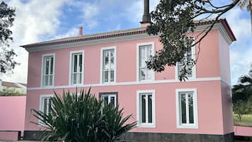Un edificio rosa con detalles blancos y numerosas ventanas, rodeado de vegetación.