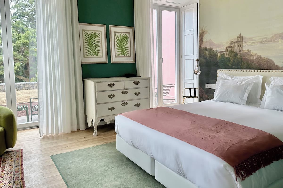 A bedroom with a bed, a dresser, a green wall, and a painting of a building.
