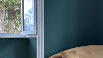 A room with a curved sofa against a teal wall, a window with a view of trees, and wooden flooring.