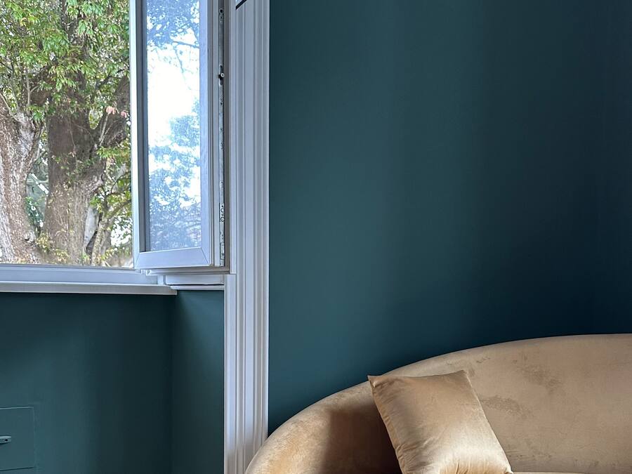 A room with a curved sofa against a teal wall, a window with a view of trees, and wooden flooring.