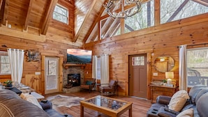 L’intérieur d’une cabane en rondins, avec une cheminée, des murs en bois, un grand canapé et un téléviseur.