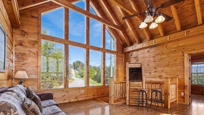 A spacious cabin with large windows, a wooden interior, a sofa, a dining area, and a ceiling fan. - The Joy Of The Mountain Tops (SEVIERVILLE)