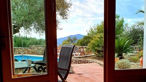 A room with a glass table, a candle, and a view of an outdoor patio with a pool, chairs, and plants. - Casa Emilia (Cómpeta)