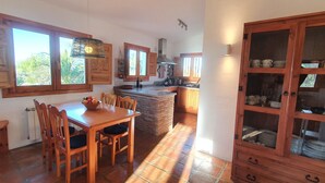 A kitchen with wooden cabinets, a dining table with chairs, and a cabinet with dishes. - Casa Emilia (Cómpeta)