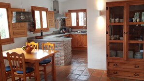 A kitchen with wooden cabinets, a brick island, and a dining table with chairs. - Casa Emilia (Cómpeta)