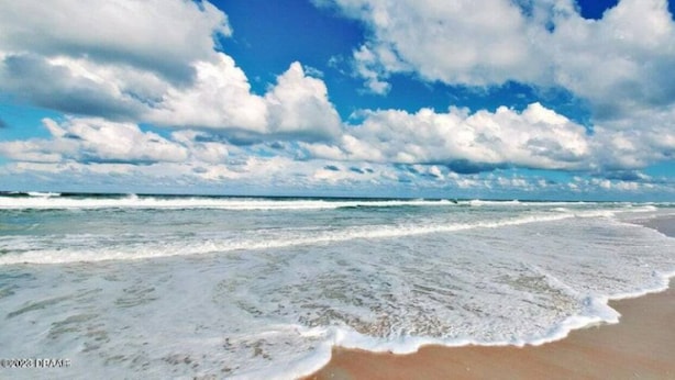 Een strand met golven, een heldere lucht en wolken.