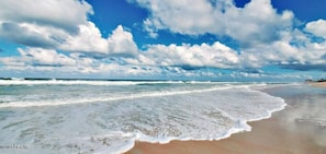 Ein Strand mit Wellen, blauem Himmel und Wolken.