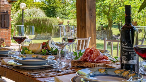 An outdoor dining table with plates, glasses, a bottle of wine, and a selection of cheeses and cured meats. - Il Pratone 12, Emma Villas (Pomarance)