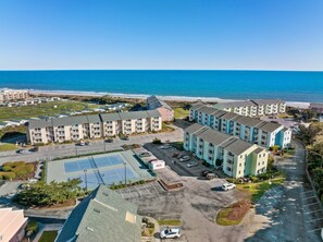 A coastal hotel with multiple buildings, a parking lot, and a view of the ocean. - Pebble Beach H212, 2BR Condo ~ Pool Front! (Emerald Isle)