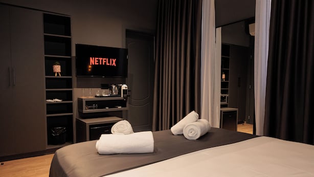 A modern hotel room with a large bed, a flat-screen TV displaying 'NETFLIX', a minibar, and a neatly made bed with towels. - Hotel Bel Ami Tirana (Tirana)