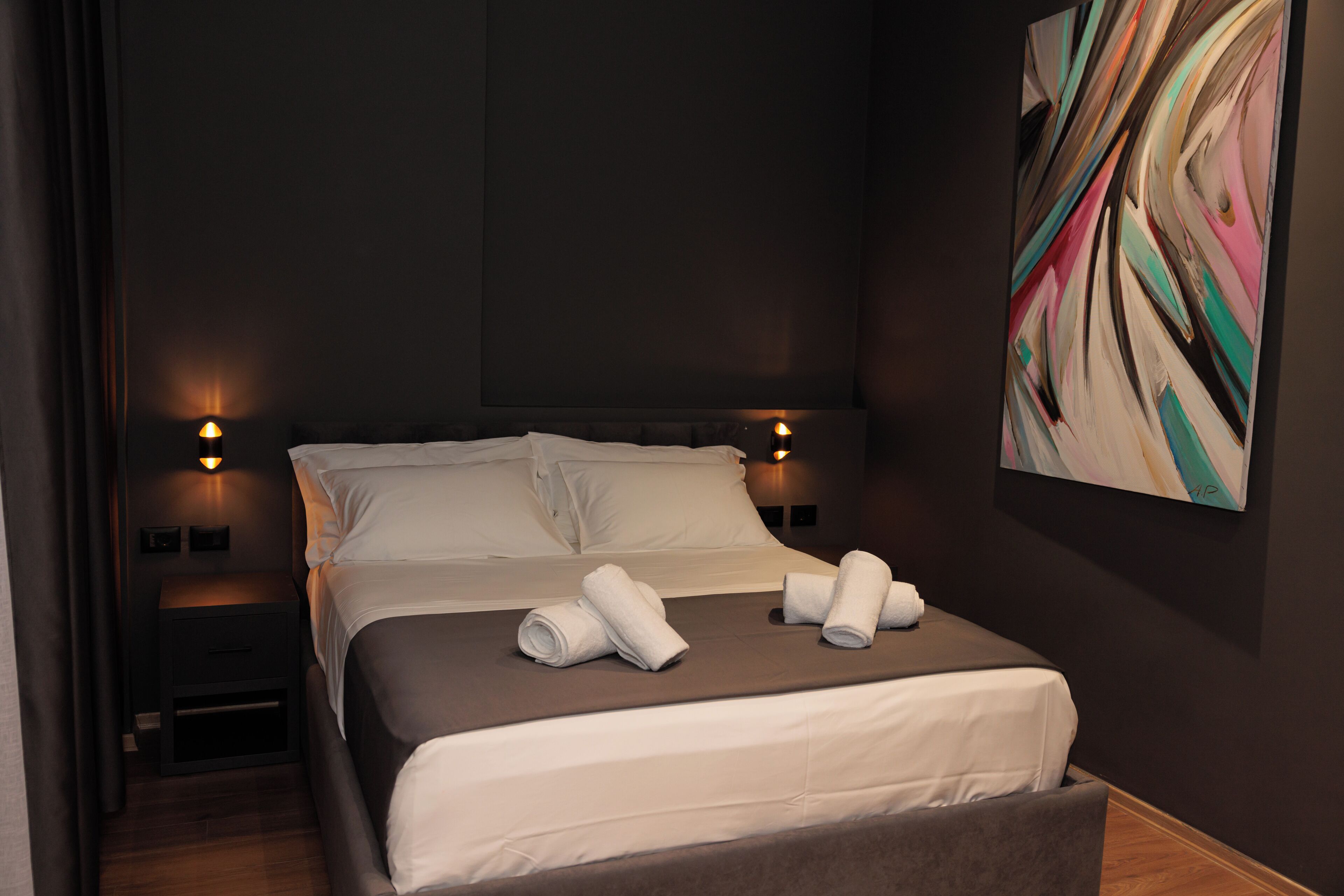 A modern hotel room with a large bed, two bedside tables, and a wall-mounted abstract painting.