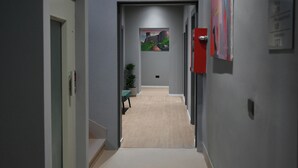 A narrow hallway with a carpeted floor, a door on the left, and a red fire alarm on the right. - Hotel Bel Ami Tirana (Tirana)