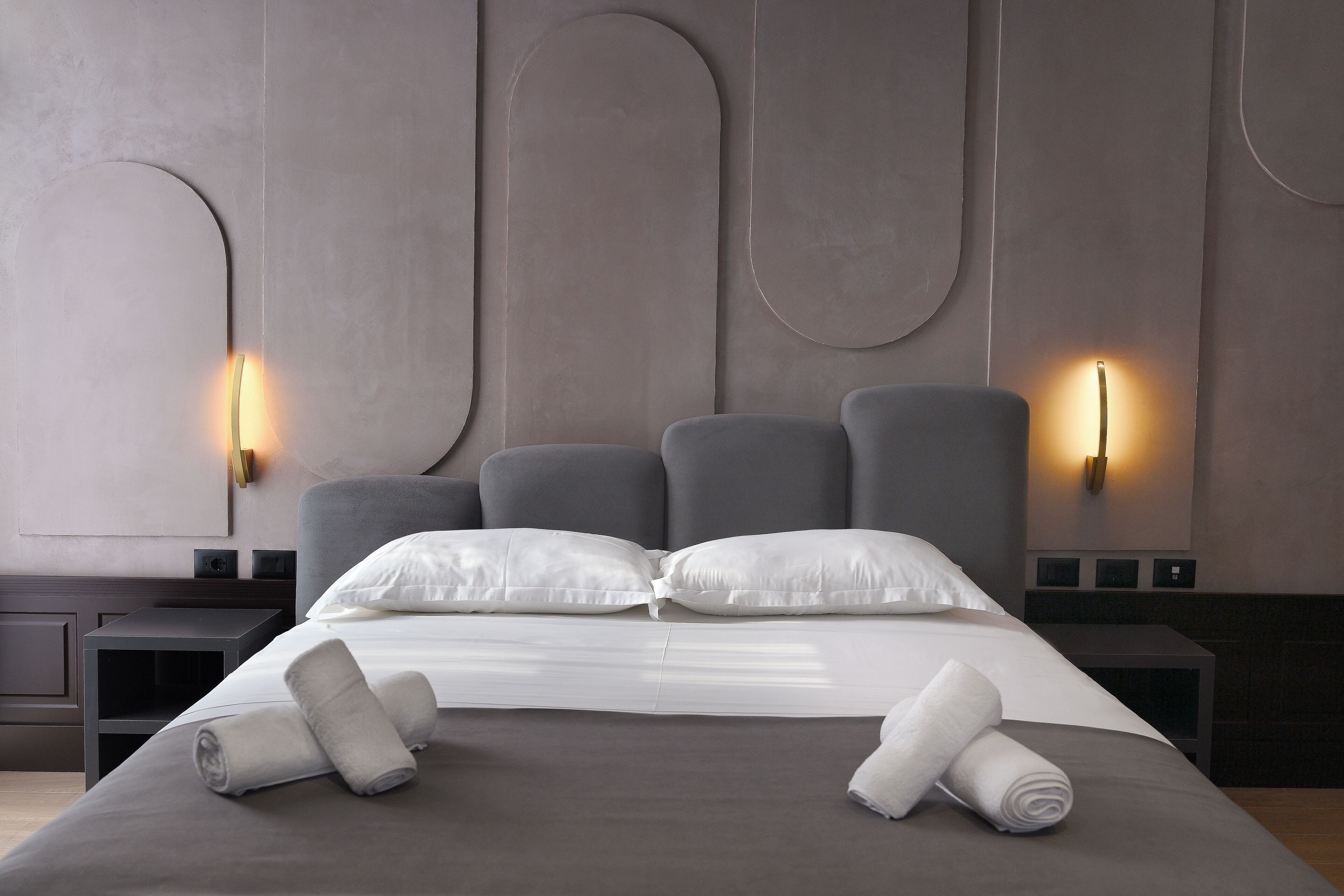 Een moderne hotelkamer met een groot bed, twee nachtkastjes en wandlampen.