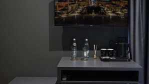 A modern hotel room with a flat-screen TV mounted on the wall, a small desk with a coffee maker, and a compact refrigerator. - Hotel Bel Ami Tirana (Tirana)