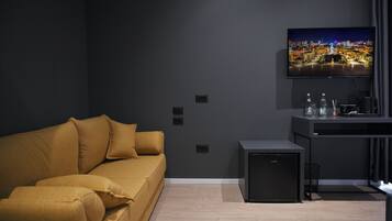 Una sala de estar moderna con un sofá, un pequeño mueble negro y un televisor de pantalla plana montado en la pared.
