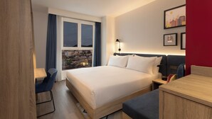 Une chambre d’hôtel moderne, dotée d’un grand lit, d’un bureau et offrant une vue sur la ville.