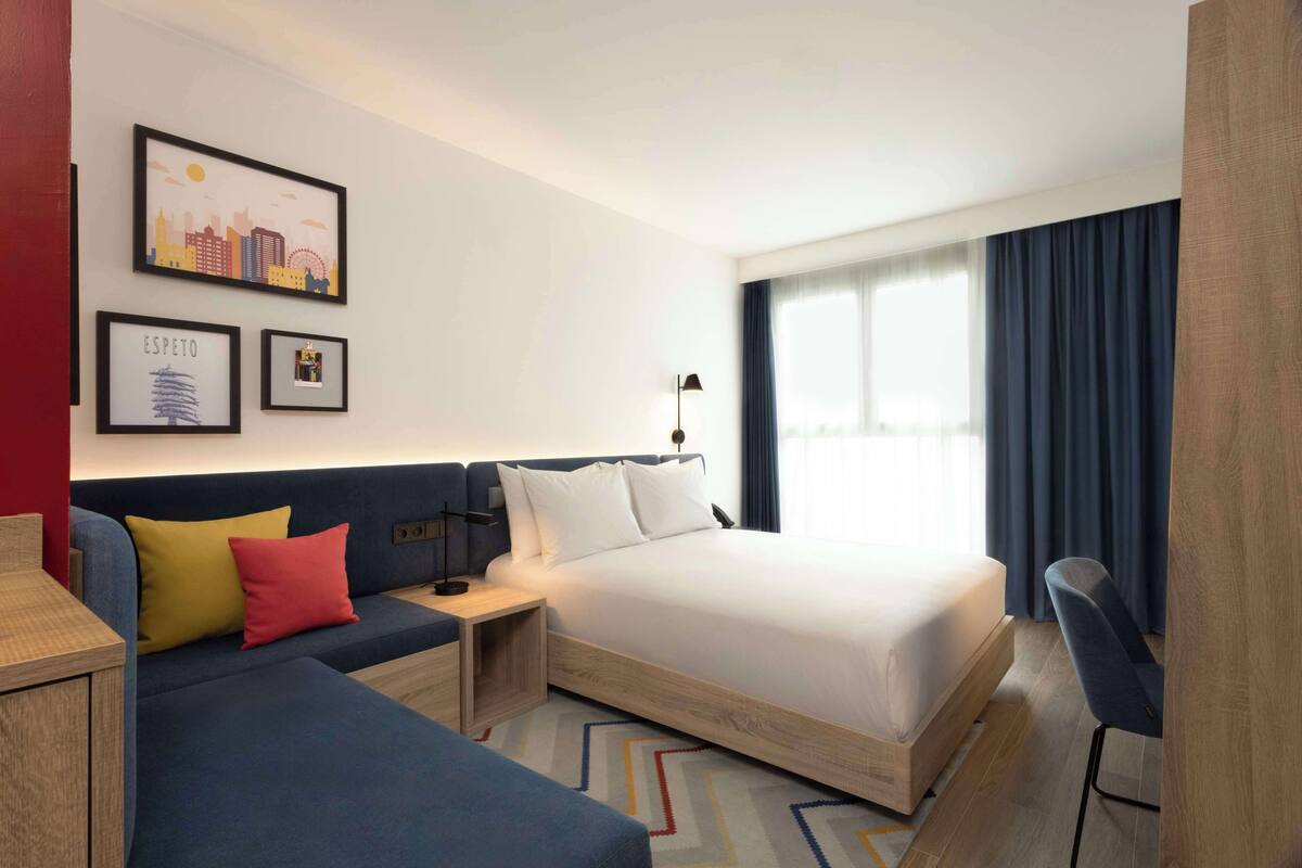 Quarto de hotel com cama, sofá, escrivaninha e cadeira. Quadros emoldurados na parede.