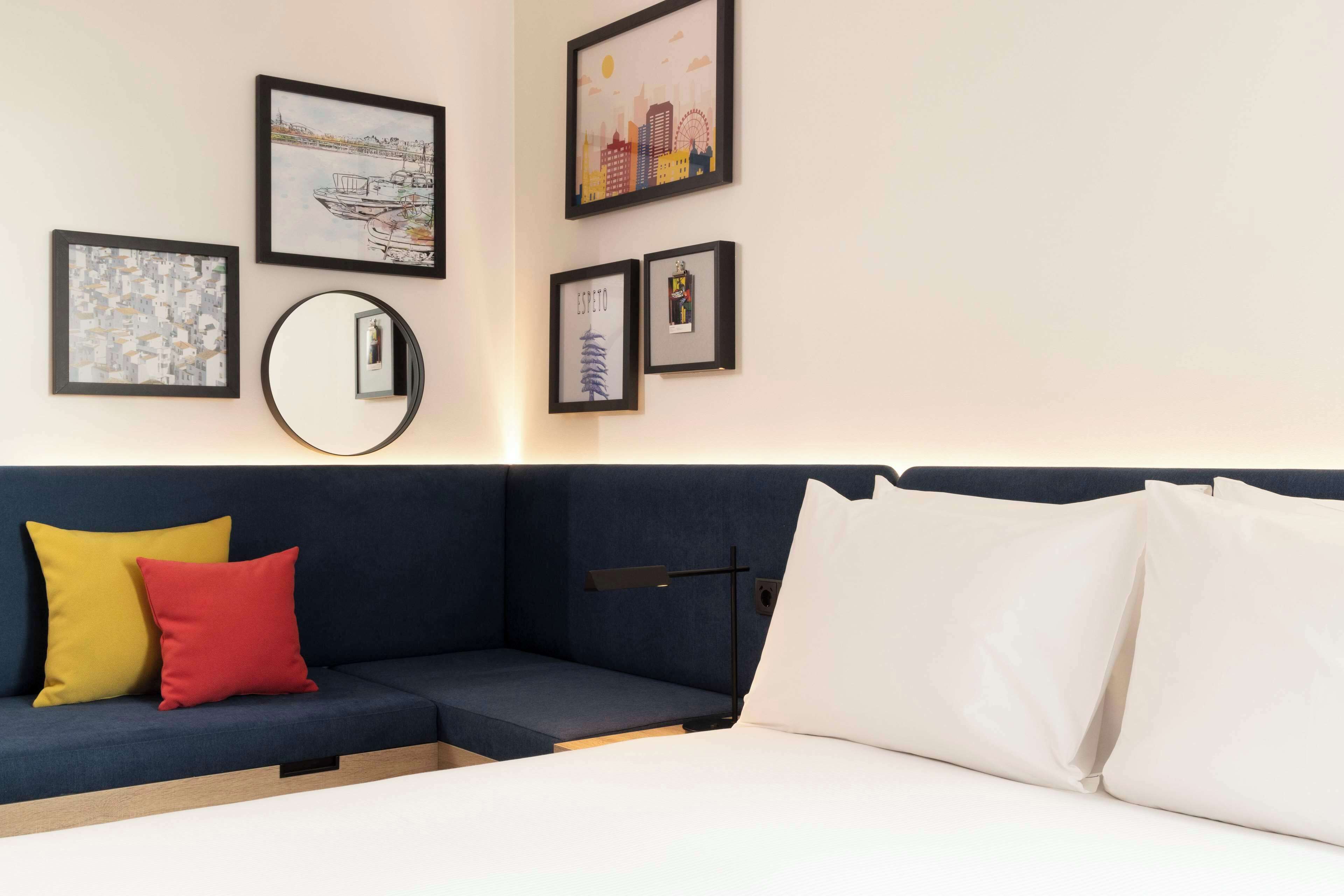 A modern hotel room with a dark blue sofa, a bed with white linens, and several framed artworks on the wall.