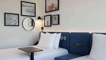 Habitación de hotel con cama, una mesita y un espejo montado en la pared. Hay cuadros enmarcados en la pared.