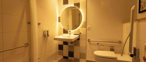 Un baño con lavamanos blanco, un espejo redondo con luz, inodoro y zona de ducha.