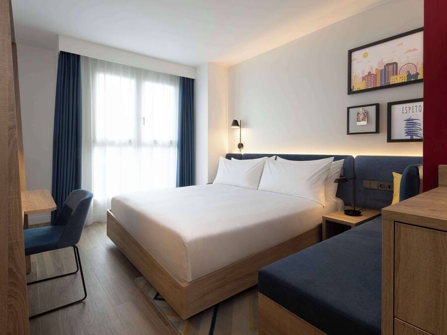 Ein Hotelzimmer mit einem Bett, einem Schreibtisch, einem Sessel, einem Nachttisch und einer Wand mit gerahmten Bildern.