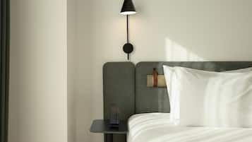 Una cama bien hecha con ropa blanca, una mesita de noche pequeña con una lámpara y un reloj de pared.