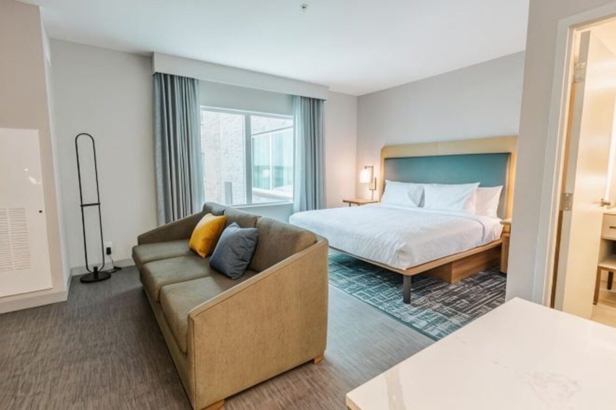 A hotel room with a bed, a sofa, a desk, and a standing lamp.