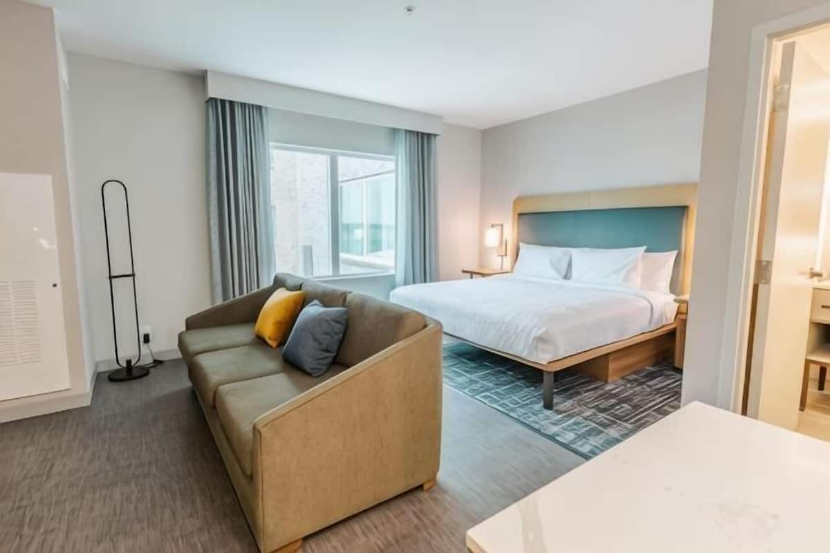 A hotel room with a bed, a sofa, a desk, and a standing lamp.
