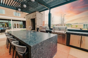 An outdoor kitchen area with a granite countertop, bar stools, a grill, and a brick oven.