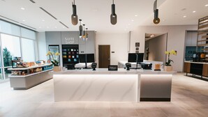 Ein moderner Hotel-Empfangsbereich mit einer weißen Rezeption, einer Minibar und einem sichtbaren 'Suite Shop'-Schild.