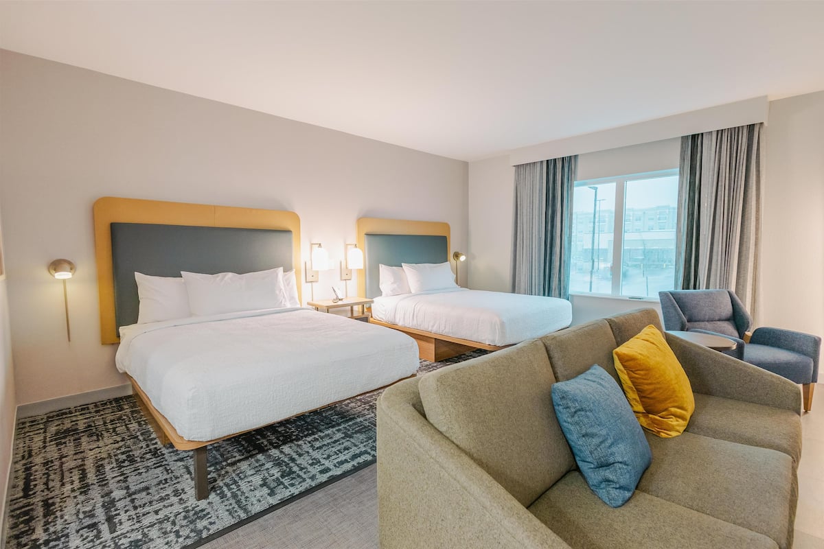 A hotel room with two beds, a sofa, a chair, and a large window with curtains.