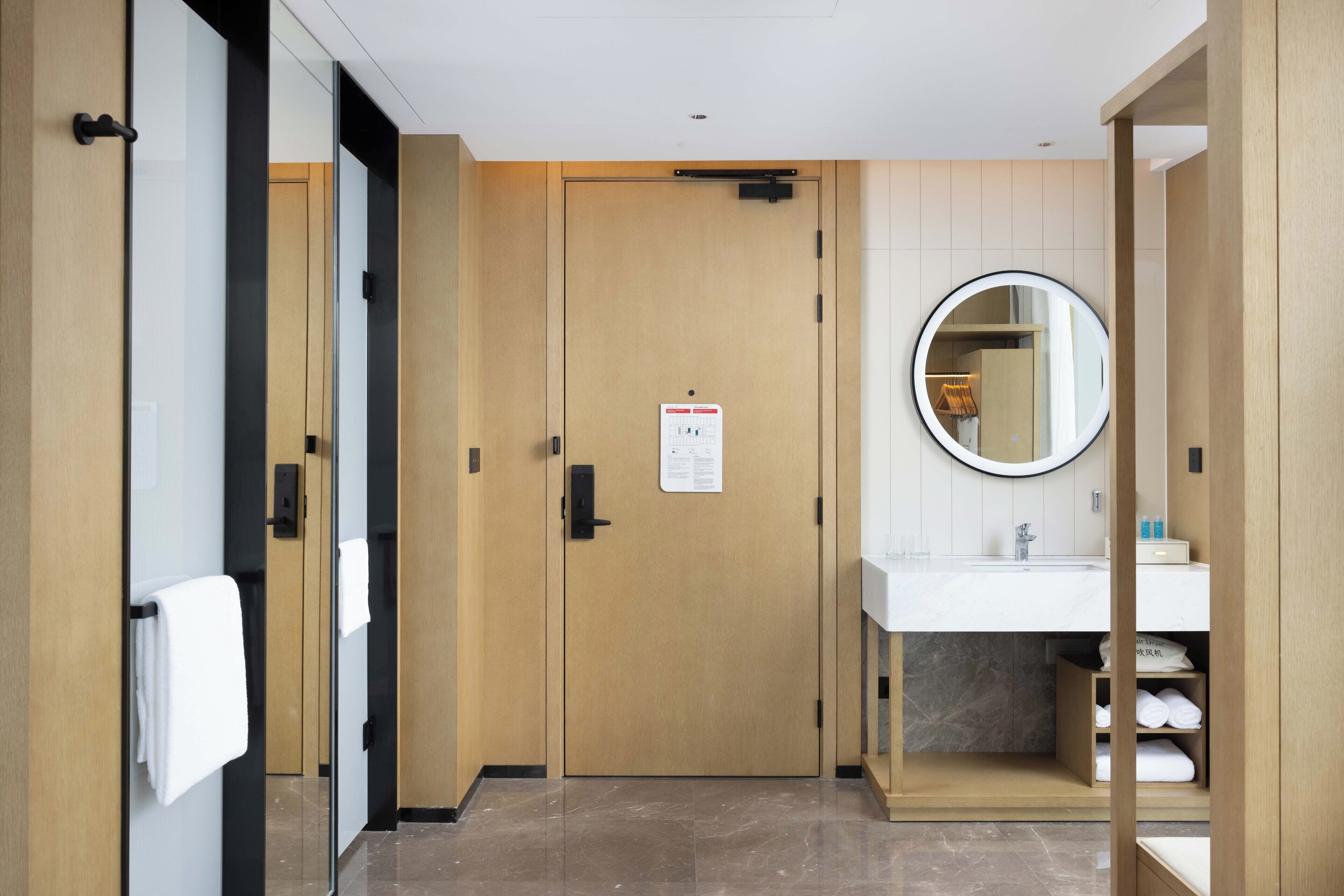 Une salle de bain d’hôtel avec une porte en bois, un miroir, un lavabo et un porte-serviettes.