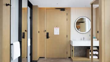 A hotel bathroom with a wooden door, a mirror, a sink, and a towel rack.