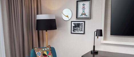 A modern room with a teal armchair, a small round table, a desk, and a large flat-screen TV on the wall.
