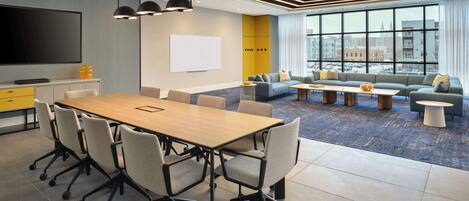 A modern conference room with a large table, chairs, a TV, and a whiteboard.