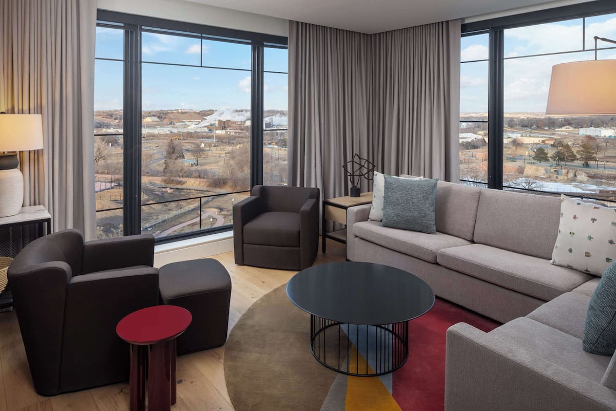 Een moderne woonkamer met een bank, fauteuils, een salontafel en uitzicht op een stadsgezicht door grote ramen.