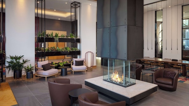 A modern lobby with a glass fireplace, seating areas, and indoor plants. - Canopy By Hilton Sioux Falls Downtown (Sioux Falls)