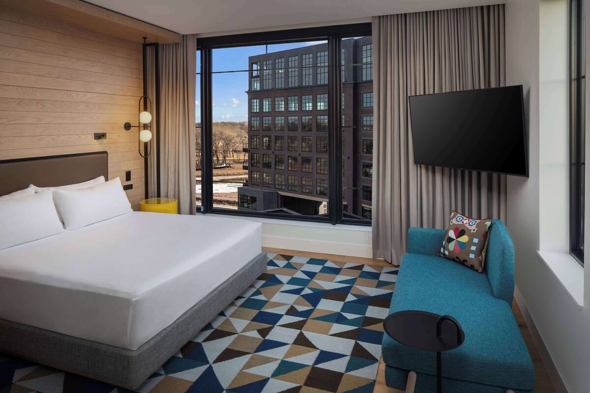 Een hotelkamer met een groot bed, een bank, een televisie en uitzicht op een gebouw.